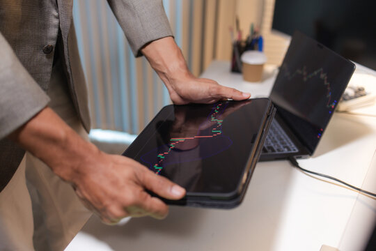 Professional financial analyst reviewing stock market charts across multiple screens using a tablet, laptop and calculator to evaluate price movements, technical indicators, and investment strategies.