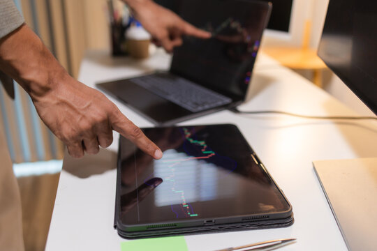 Professional financial analyst reviewing stock market charts across multiple screens using a tablet, laptop and calculator to evaluate price movements, technical indicators, and investment strategies.