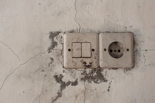 Old and Dirty Light Switches on a Worn Wall. A close-up shot of old, yellowed, and dirty electric light switches with a power socket on a stained white wall.