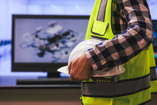 Construction worker in a safety vest holding a hard hat with a drone image on a screen in the background
