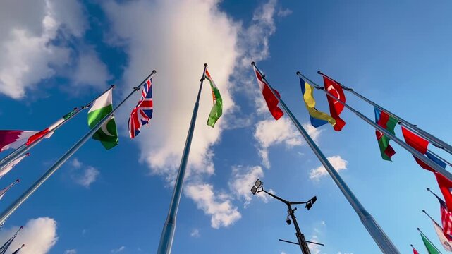 International national flags including United Kingdom, Ukraine, Turkey and India waving in strong wind against blue sky with clouds. Global unity, international relations, and diplomacy concept