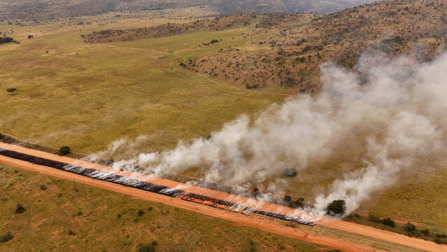 Aerial view of a controlled fire burning along a dirt road through the dry savanna landscape in Vaalwater, Limpopo, South Africa.