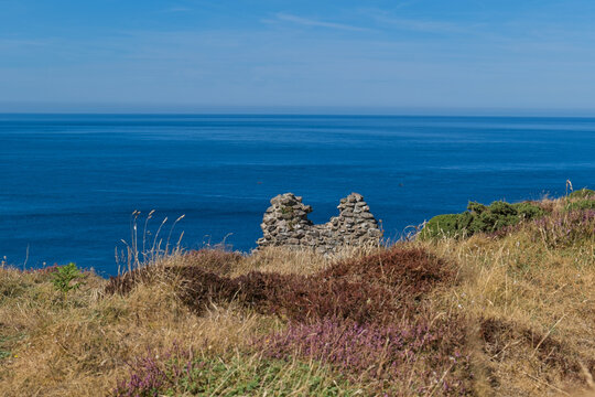 ancient stone ruins on a grassy, heather-covered cliff overlooking a vast, deep blue ocean under a clear sky - Jacob's Mine, Botallack, Cornwall, UK