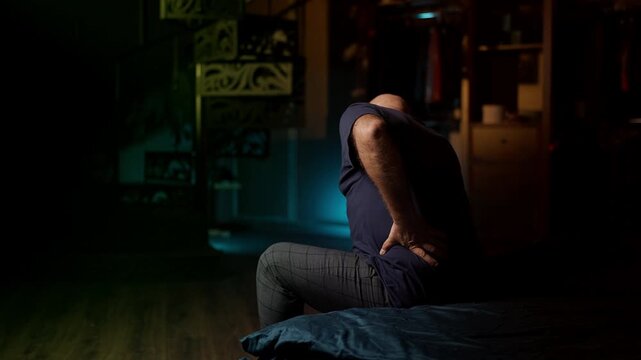 Upset middle-aged man feels sudden lower back pain while sitting on the sofa