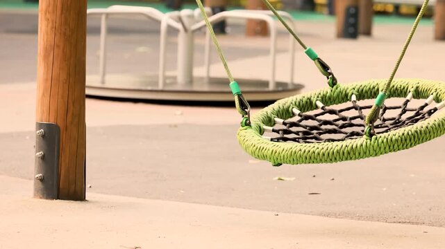 Nest swing on a Dubai style urban playground with a green rope wrapped steel frame and woven black mesh seat rocks gently back and forth, showing modern Gulf city park recreation infrastructure.