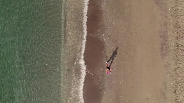Athletic woman training kick boxing on the beach with waves from an aerial drone top down view in summer