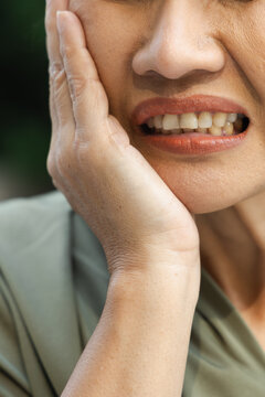 asian middle aged woman suffering from toothache and tooth decay outdoors, holding her cheek in pain, dental care concept, body parts closeup shot