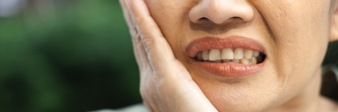 asian middle aged woman suffering from toothache and tooth decay outdoors, holding her cheek in pain, dental care concept, body parts closeup shot