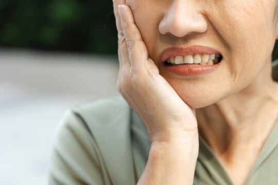 asian middle aged woman suffering from toothache and tooth decay outdoors, holding her cheek in pain, dental care concept, body parts closeup shot