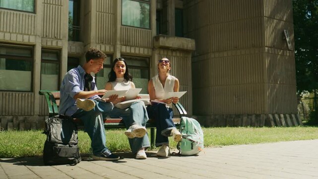 High school students are collaborating on a bench outside, engaged in their studies. Young friends discuss their schoolwork outdoors on a bright day.