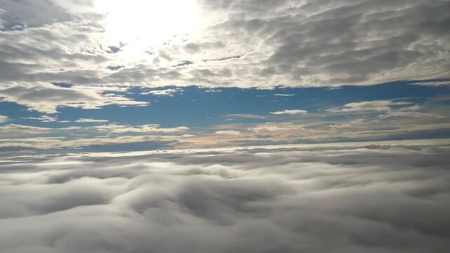 Aerial View Above a Sea of Fluffy White Clouds with Sunlight Breaking Through Blue Sky