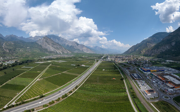 Aerial view of the A9 highway cutting through agricultural fields and the industrial zone near the River Rhone in Riddes, Valais, Switzerland.