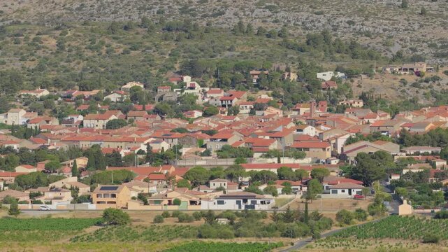 The village of Opoul Perillos in southern France, featuring traditional Mediterranean houses with red-tiled roofs nestled among green vegetation and surrounded by rocky hills, aerial view.
