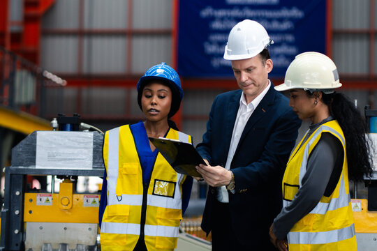 Industrial teamwork and digital manufacturing. Engineers review production data using a laptop and tablet beside factory machinery. Industry, teamwork, technology, inspection, production