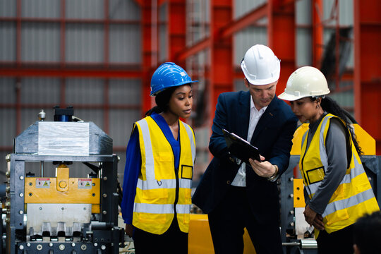 Industrial teamwork and digital manufacturing. Engineers review production data using a laptop and tablet beside factory machinery. Industry, teamwork, technology, inspection, production