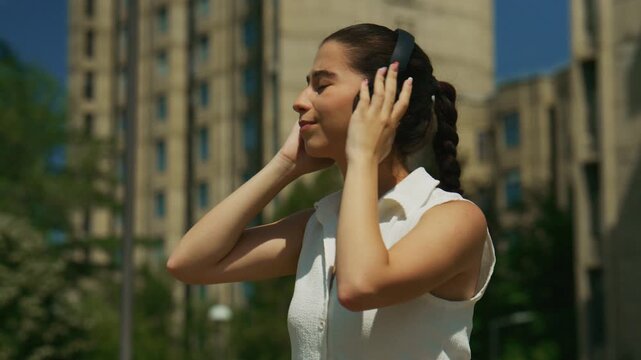 A high school student puts on wireless headphones to enjoy music outdoors. She relaxes, immersed in sound.