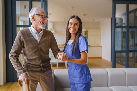 Young female nurse helping senior man stand with wooden stick at home, caregiver assisting elderly patient with mobility support, rehabilitation and healthcare service concept with copy space