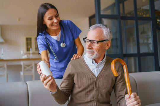 Female nurse giving pill jar to senior man at home, caregiver assisting elderly patient with medication, healthcare support, home care service and treatment concept