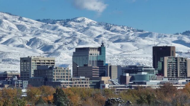 Aerial view of the downtown Boise skyline set against snow-covered mountains under a clear blue sky in Boise, Idaho, United States.