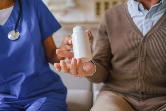 Close up of female nurse giving pill jar to senior man at home, caregiver assisting elderly patient with medication, healthcare support, home care service and treatment concept