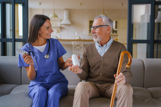 Female nurse giving pill jar to senior man at home, caregiver assisting elderly patient with medication, healthcare support, home care service and treatment concept