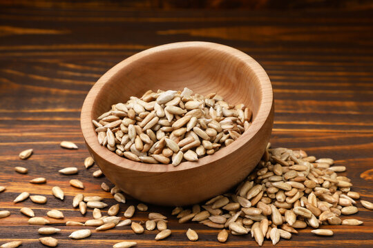 Roasted sunflower seed kernels in a bowl and scattered on a wooden background.