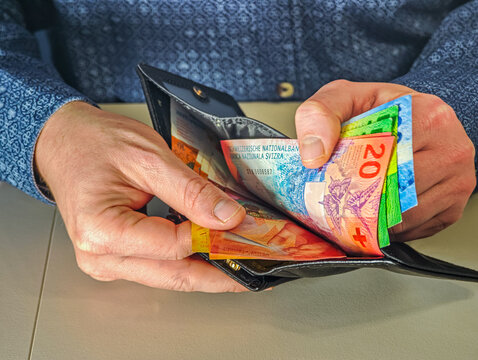 Man putting Swiss Franc banknotes into black leather wallet close up, financial success concept