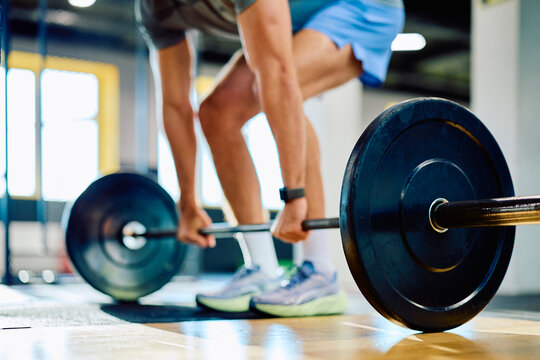 Male athlete performing a deadlift, gripping a heavy barbell on the floor, focusing on strength training and fitness