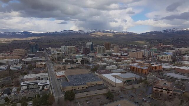 Aerial view of the downtown Boise skyline featuring modern buildings and urban streets set against a backdrop of distant mountains under a cloudy sky in Boise, Idaho, United States.