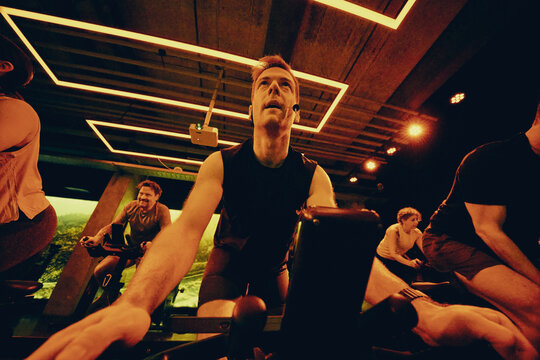 Spin class instructor leading an intense indoor cycling workout in moody studio lighting
