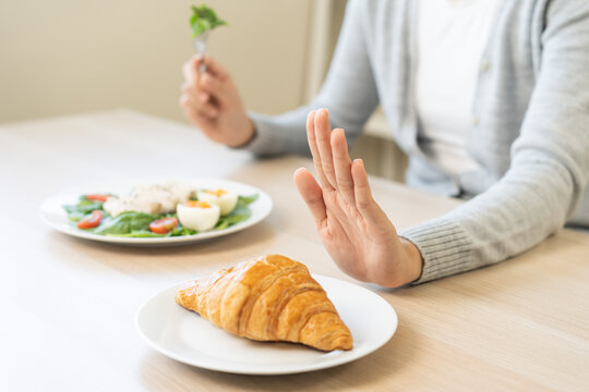 Ketogenic, Low carb, Intermittent Fasting diet woman push out, deny hand push out, deny butter croissant bread on plate, choose green vegetable salad, eat food for good healthy, getting weight loss.