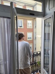 Man looking out from the open balcony door of a European apartment on a summer morning