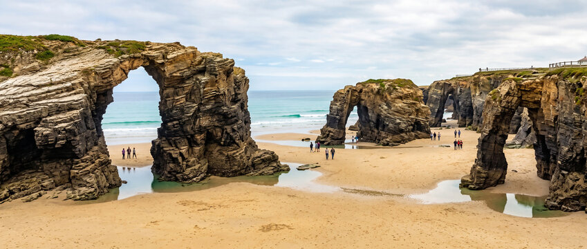 Natural rock formations at the beach with people exploring the shoreline in Galicia, Spain