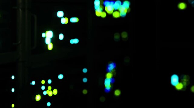 Workers carry out tasks in a data center filled with glowing lights at night. The scene shows various colors shining in the dark space. Some areas are brighter while others are dim.