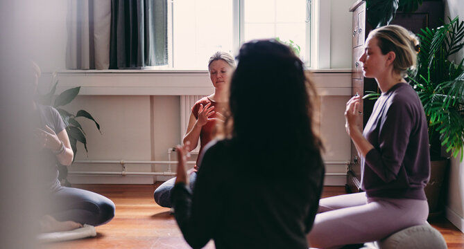 Women meditating in a restorative yoga class. They are sitting in a circle with their eyes closed, focusing on their breathing and meditation.