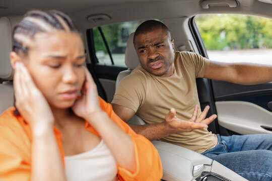 Young African American couple arguing inside car, frustrated man gesturing angrily while stressed woman covers her ears, illustrating relationship conflict and tension