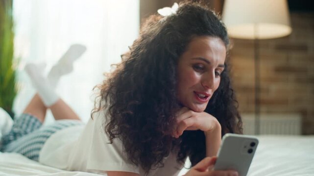 Happy Caucasian woman talking video call with mobile phone at cozy bed at home morning optimistic female girl talk smartphone conference chatting conversation virtual app chat at comfortable bedroom