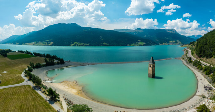 Aerial drone panoramic view of the historic flooded bell tower in Lake Reschen surrounded by mountains, Curon Venosta, South Tyrol, Italy.