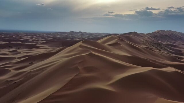 Aerial view of vast sand dunes of the Gobi Desert under a dramatic cloudy sky in Mongolia.