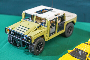 Fototapeta premium Large, robust tan and black Lego jeep with visible interior, flanked by smaller yellow cars on a green surface Bright lighting accentuates colors and textures - Kyiv, Ukraine - June 7, 2025
