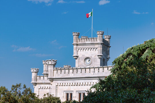 The white stone tower of Miramare castle with Italian flag against blue sky in Trieste, Italy