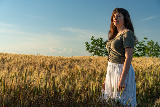 Young woman in white skirt standing in golden wheat field during sunset