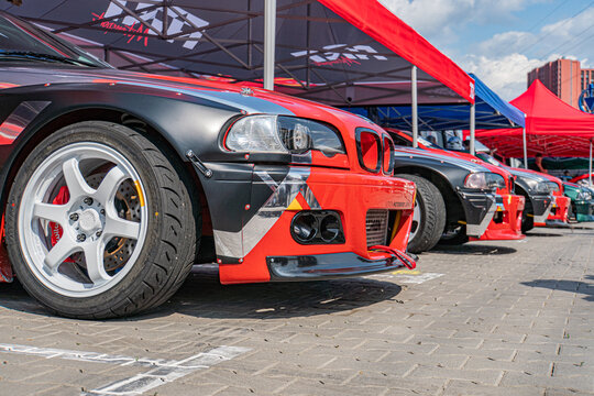 Red BMW E30 M3 with black and white graphics at a car show, under red tents, amidst other parked cars Sunny day setting - Kyiv, Ukraine 06-15-2025
