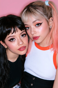 two women of different backgrounds flirting in stylish alternative fashion, two diverse women sharing a playful romantic moment, multicultural women with colorful hair and glossy makeup