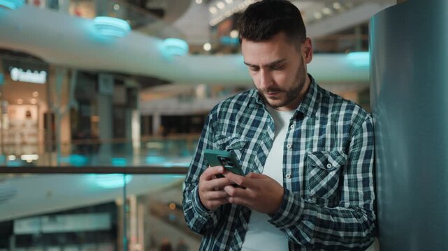 Concentrated gadget addicted Caucasian business man using mobile phone guy choosing online goods with black friday discount in shop store male client with smartphone focused chatting in shopping mall
