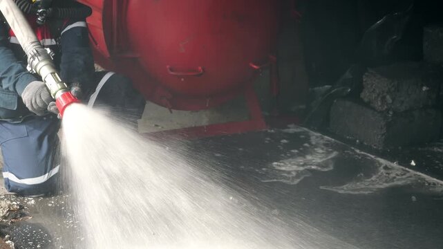 Firefighter operates a fire hose nozzle, spraying a powerful stream of water during firefighting. Emergency response, fire suppression and rescue operation.