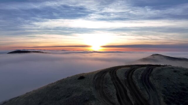 Aerial view of Bogus Basin at sunset with rolling hills and dirt tracks rising above a sea of clouds in Boise County, Idaho, United States.