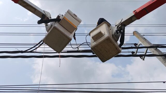 Two professional linemen in dual bucket trucks working together to joint twisted aerial cable.