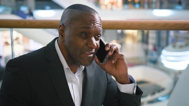 Serious ethnic African American business man pensive discussing problem with mobile phone talk indoors mature businessman male professional discuss trouble difficulties talking smartphone in company