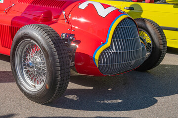 Fototapeta premium Vintage Alfa Romeo Formula 1 car on tarmac racetrack, red with white and yellow accents, round headlights, wire-mesh grille, large spoked wheels, daylight, - Kyiv, Ukraine - September 21, 2025